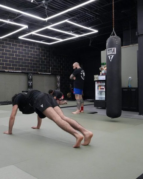 Members doing conditioning work on the mats beside a heavy bag