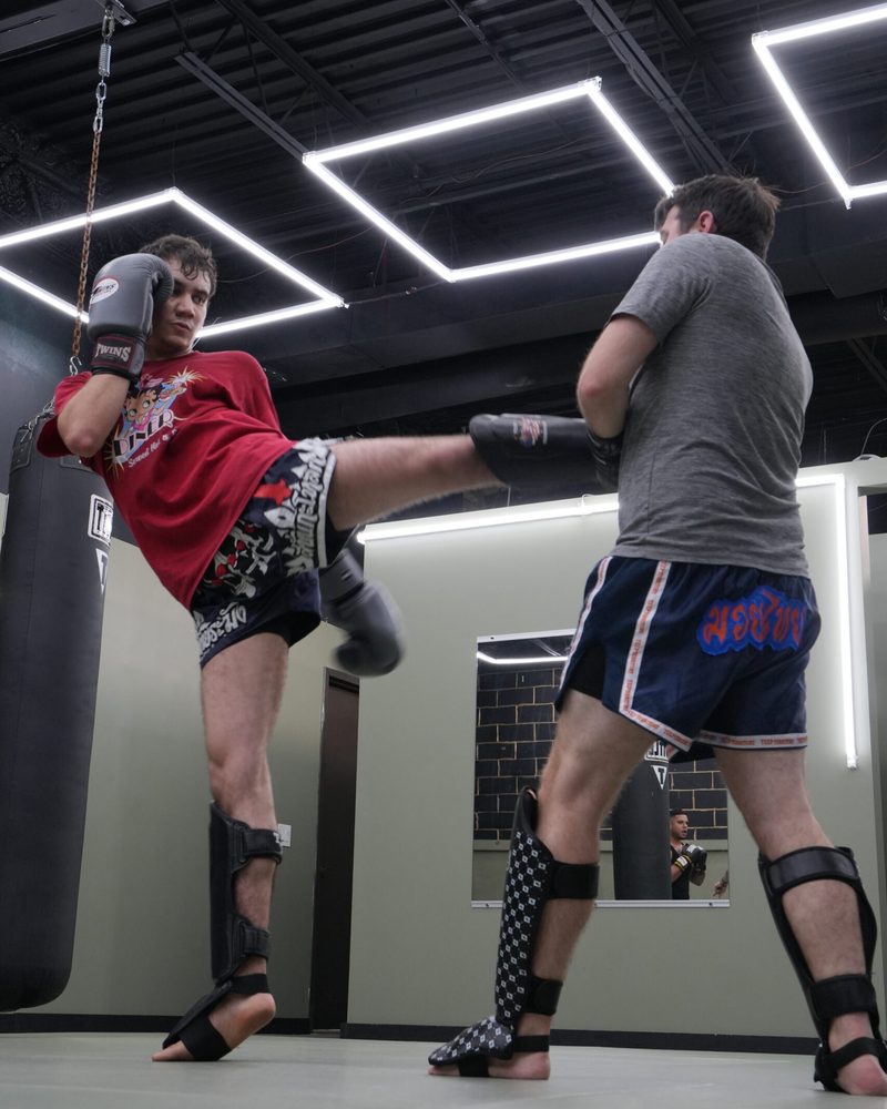 Two members drilling Muay Thai kicks under the gym's LED lights