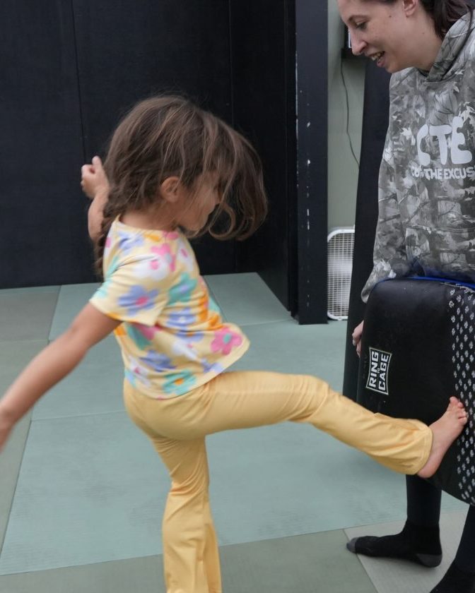 A young student throwing a kick into a coach's pad