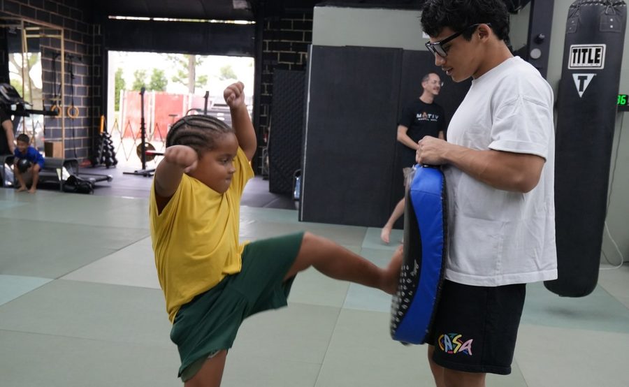 A youth student throws a kick into a pad held by a coach